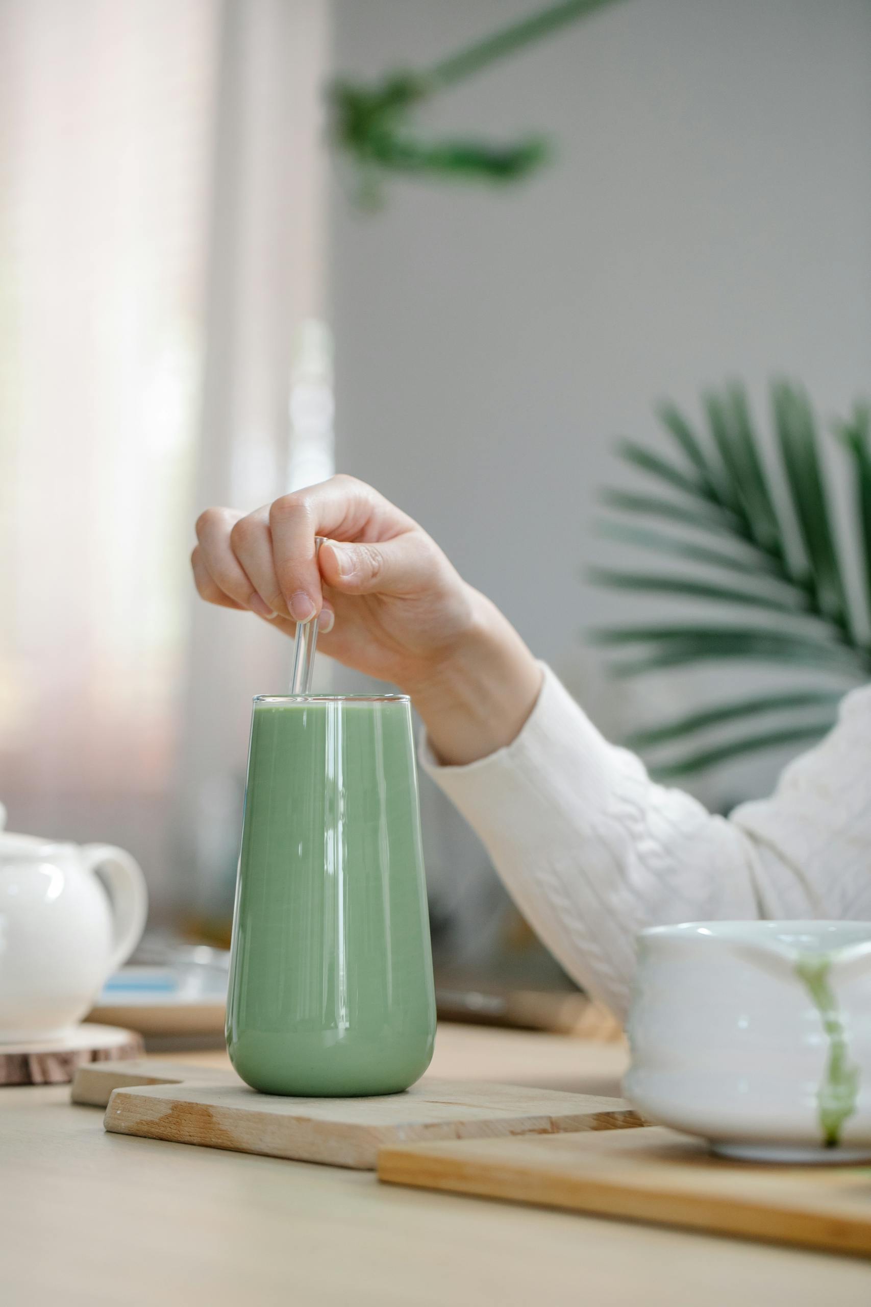 Person Stirring Matcha Drink in Clear Glass